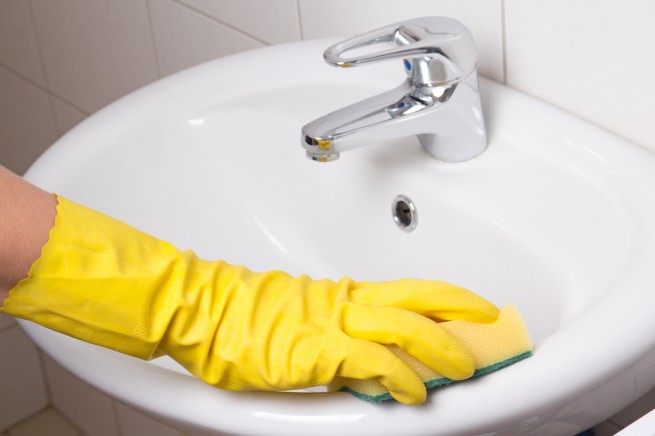 Hand in yellow glove with sponge cleaning sink
