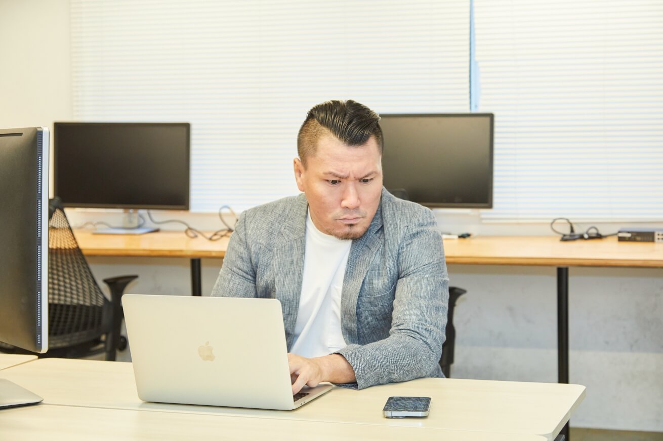 ノートパソコンで作業をしながらスマホを見ているビジネスマン